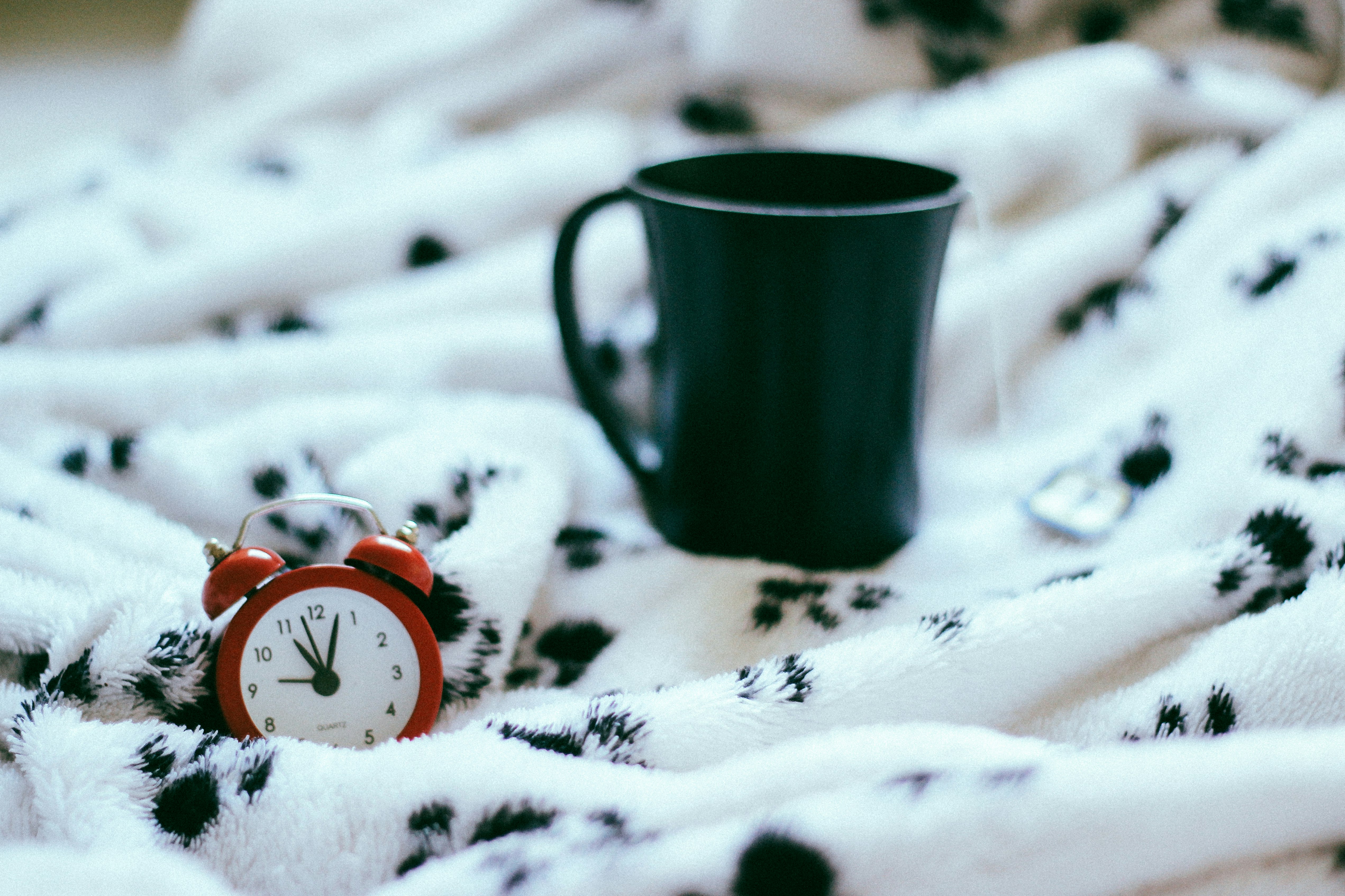 green ceramic mug near analog alarm clock